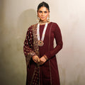 A woman wearing a maroon polyester 3-piece churidar set with long-sleeve top, matching bottoms, and a printed dupatta.