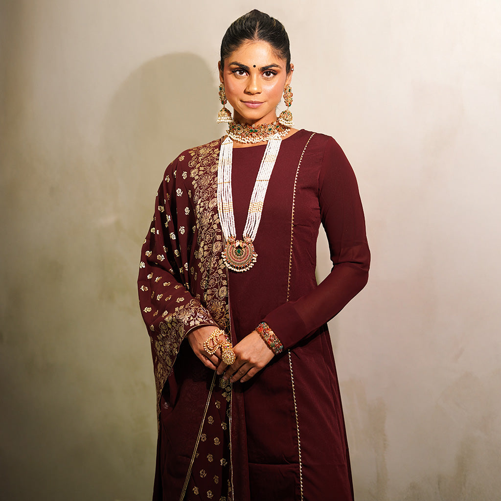 A woman wearing a maroon polyester 3-piece churidar set with long-sleeve top, matching bottoms, and a printed dupatta.